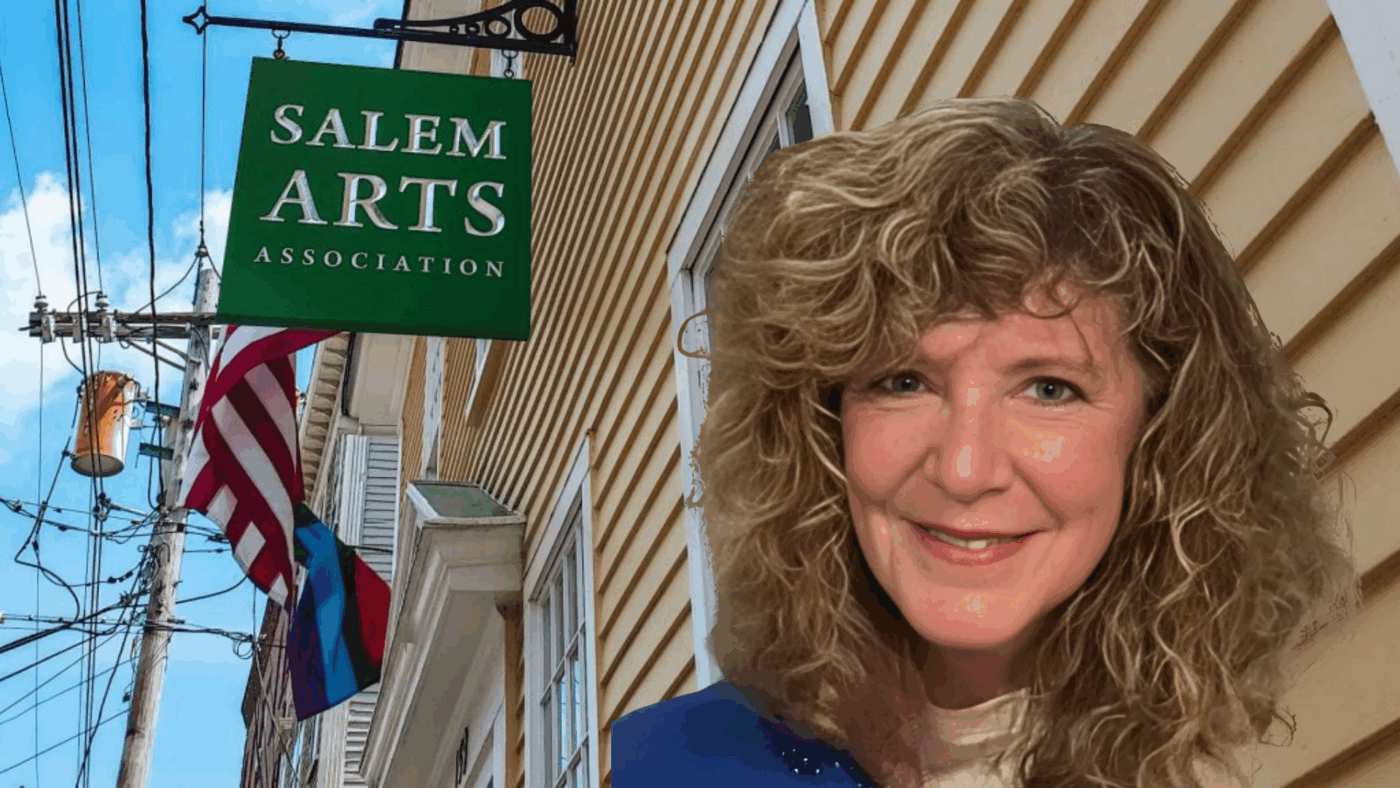 A joyful woman with curly hair beams outside our bright yellow Salem Arts Association, framed by vibrant flags and local pride.