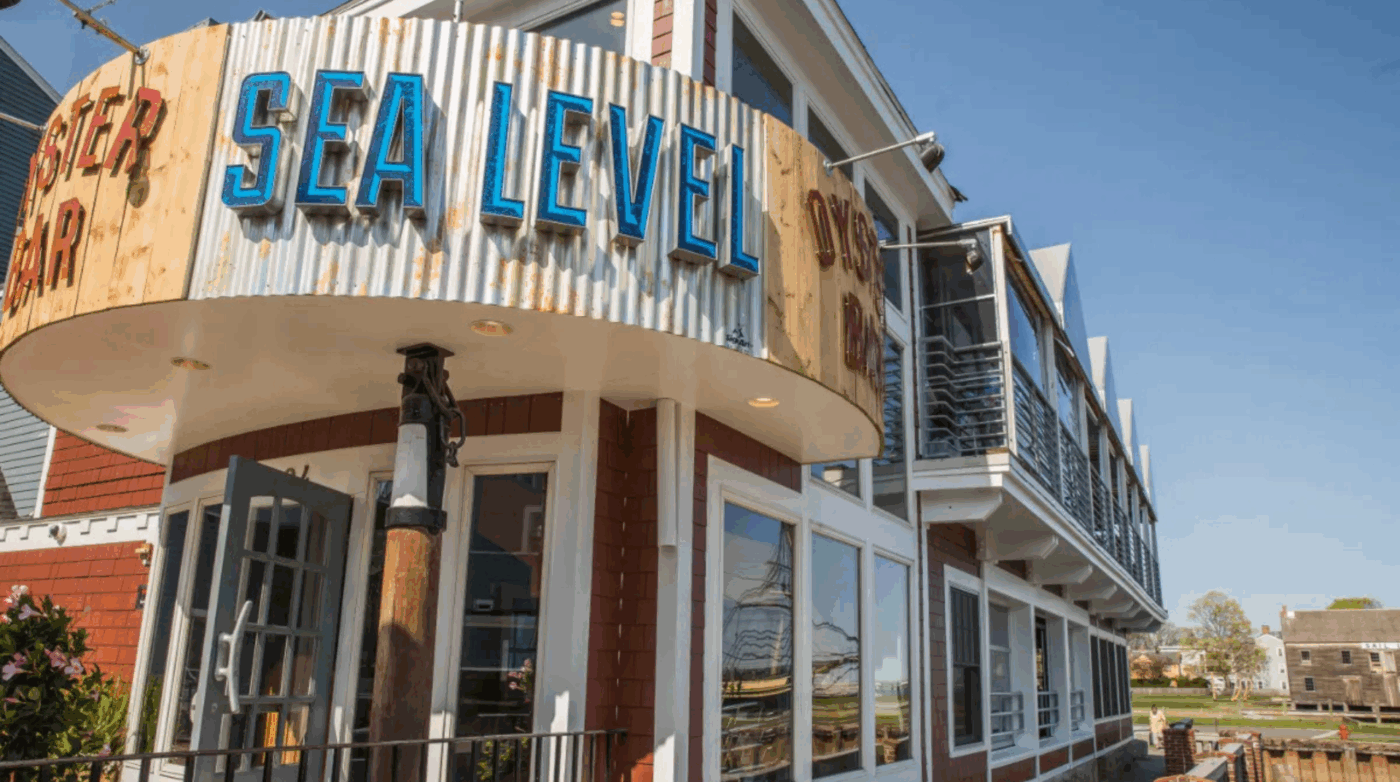 Sunny corner home to SEA LEVEL, our bright blue sign welcomes you to a vibrant, nautical spot with red brick and lively patio energy.