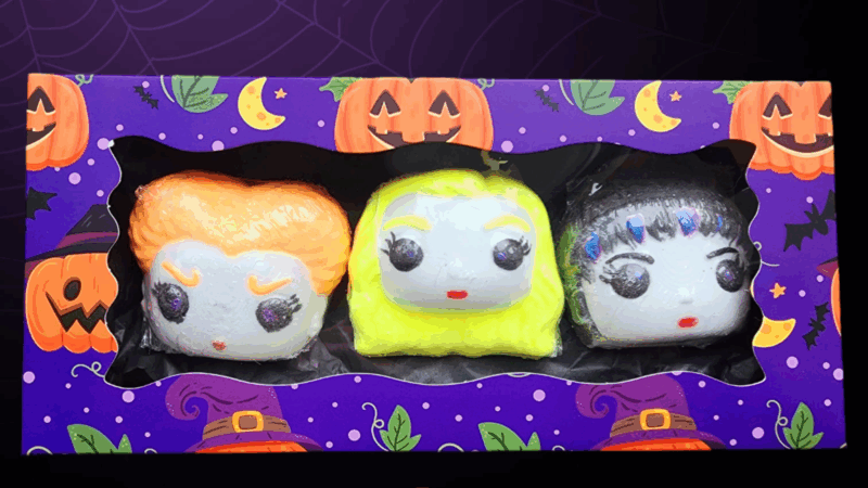 Three playful Halloween marshmallow faces with bright candy hair, in our purple box covered in pumpkins and witchy designs—crafted with local creativity.