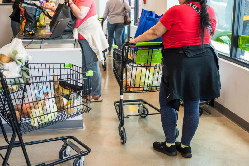 Customers line up at our sunlit checkout, carts brimming with fresh finds—neighbors chatting as local energy fills the air.