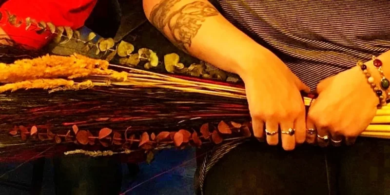 Sure! Here’s a more engaging, community-focused alt text based on your guidelines: Hands adorned with bold rings and bracelets cradle vibrant dried blooms—striped sleeves and artistic tattoo radiate our creative spirit.