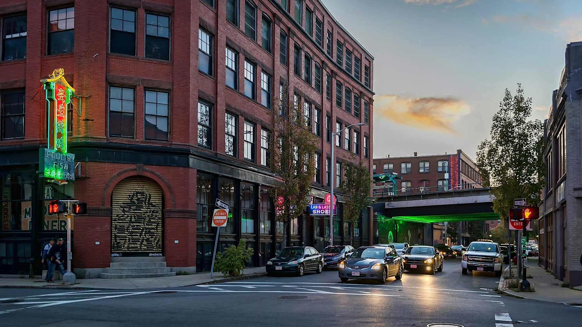 Bustling dusk street in Essex County with lively cars, glowing neon signs, and neighbors under lit trees beside a vibrant red brick hub.