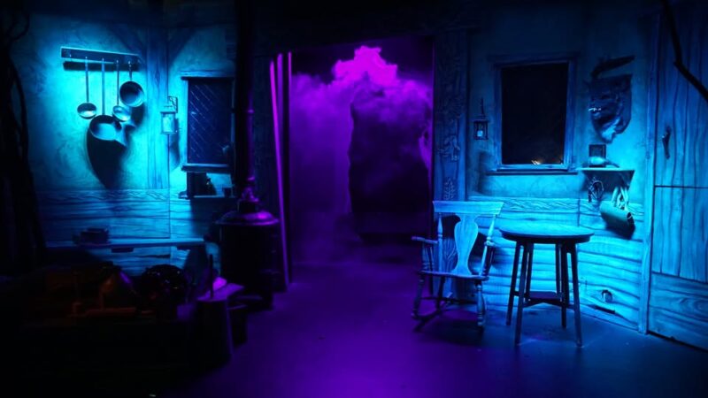 Sure! Here’s a revised, SEO-friendly, community-focused alt text: A cozy room glows with blue and purple light—rustic tables, hanging pans, and swirling mist welcome our creative community. Let me know if you’d like further tweaks or if there are local artists/creators in the image for an even tighter focus on collective energy!.