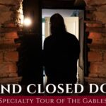 An enthusiastic visitor stands in a cozy brick doorway, inviting all to the “Behind Closed Doors” Gables tour, uniting Essex County.