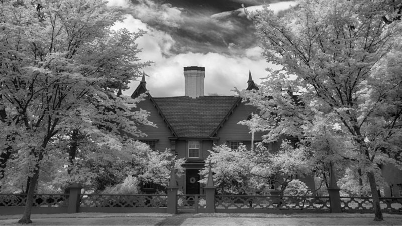A striking two-story house with a steep roof and central chimney stands among tall trees, a proud symbol of Essex County’s creative spirit.