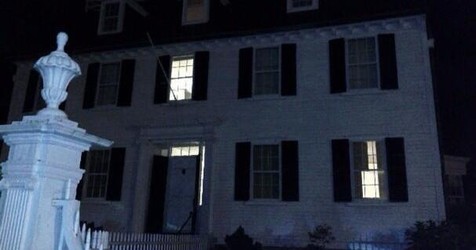 A warmly lit two-story white house with black shutters glows at night in Essex County, inviting community gatherings and creative energy.