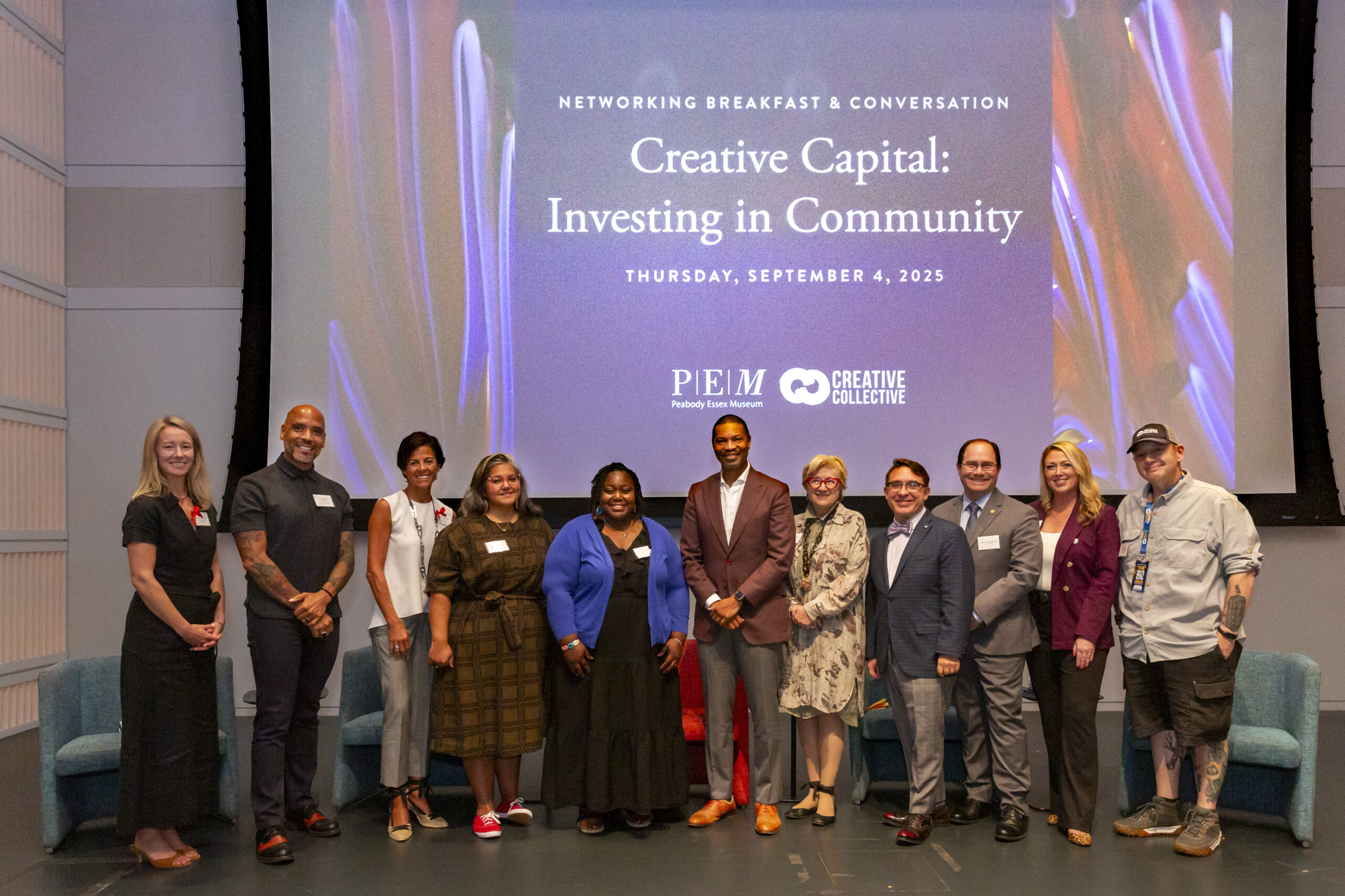 A lively group of twelve pose on stage, celebrating creative collaboration for Essex County at "Creative Capital: Investing in Community," Sept 4, 2025. Peabody Essex Museum