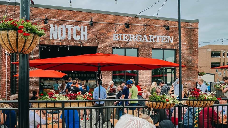 Neighbors mingle outside Notch Biergarten, vibrant with red umbrellas and blooms—a creative Essex County hub alive with connection.