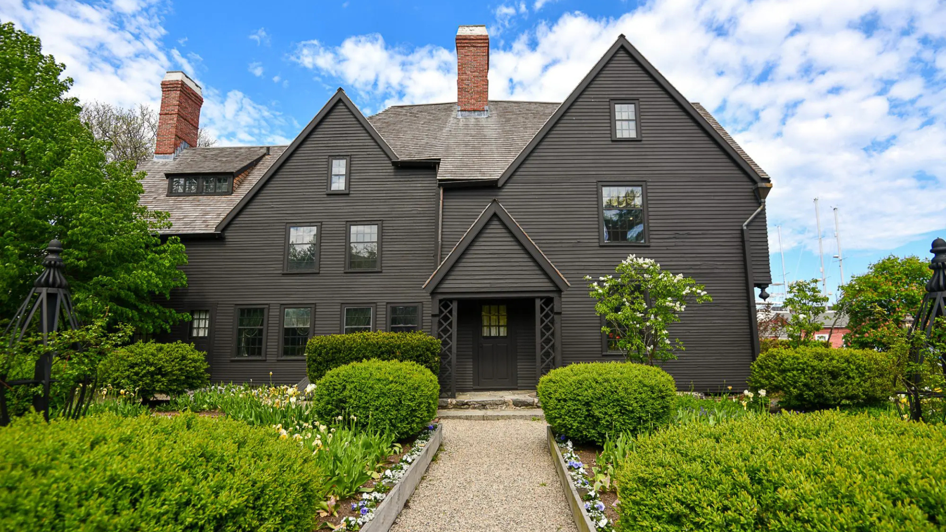 A vibrant, historic wooden house with peaked roofs and brick chimneys welcomes Essex County neighbors along a lively gravel path.