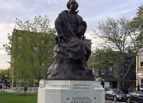 Bronze statue of Nathaniel Hawthorne on a stone pedestal in a lively park, celebrating creativity and heritage in Essex County.
