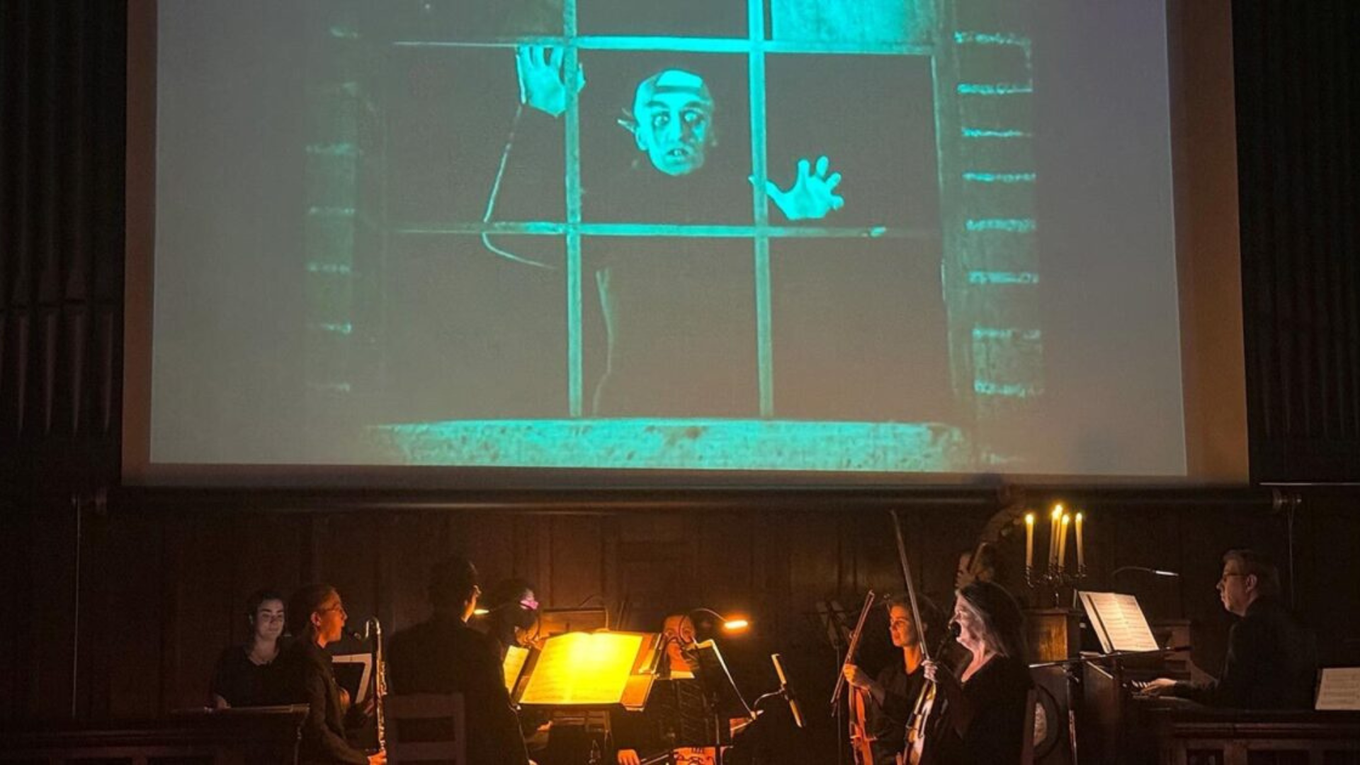 Local musicians energize the stage, uniting our Essex County crowd beneath a haunting horror film scene, candles glowing bright.