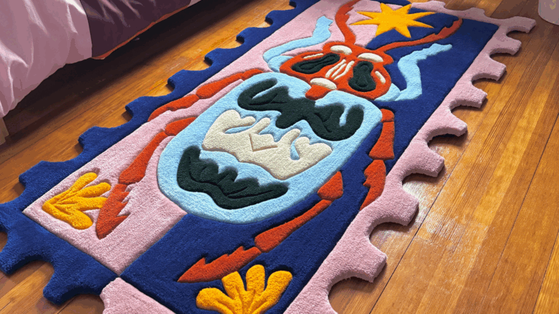 A vibrant, puzzle-edged rug with abstract blue, red, orange, yellow, black, and pink shapes brightens a wooden floor—spreading creative energy and Essex County community spirit.