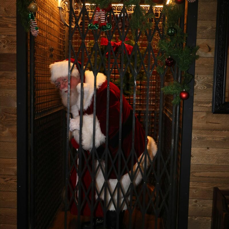 Santa Claus stands joyfully in a vintage elevator decked with lively greenery, ribbons, and ornaments, sparking Essex County holiday cheer.