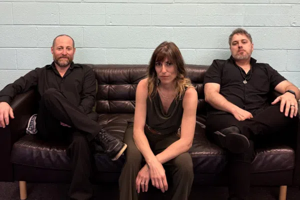 Three creative locals connect on a sleek black couch, sharing ideas and energy against a vibrant blue wall—Essex County pride!.