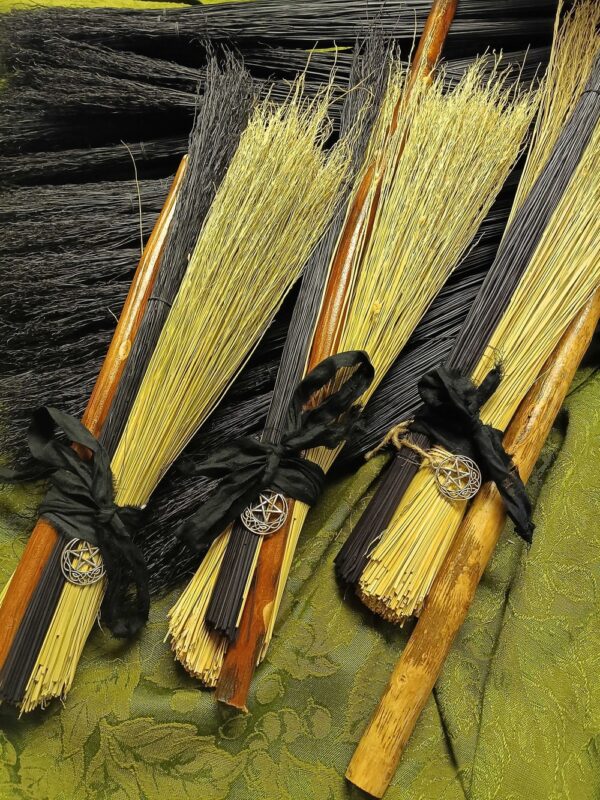 Vibrant handmade besom brooms, crafted with black-yellow bristles and pentagram charms, celebrate Essex County’s creative spirit.