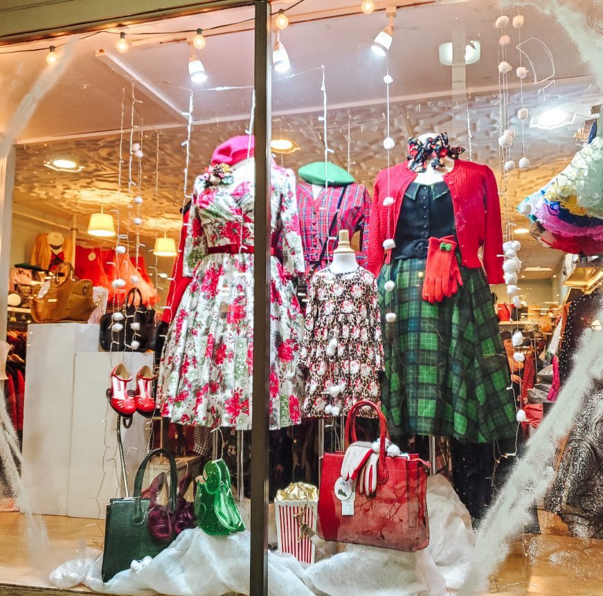 A vibrant shop window glows with vintage holiday outfits, uniting our Essex community in festive style and creative spirit.
