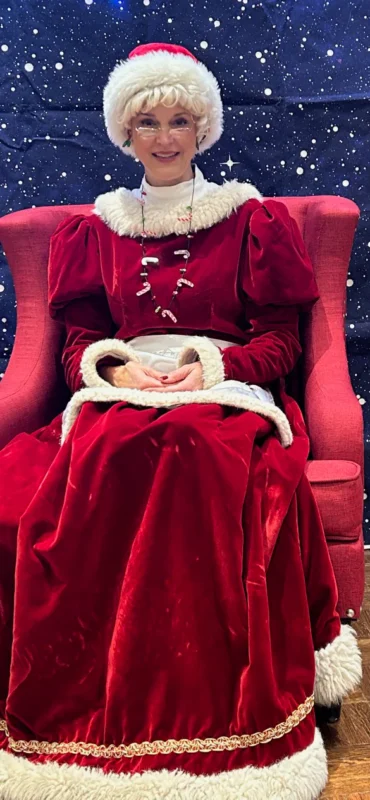 Mrs. Claus, dazzling in red velvet and sparkling beads, brings festive joy to Essex County on a starry night backdrop.