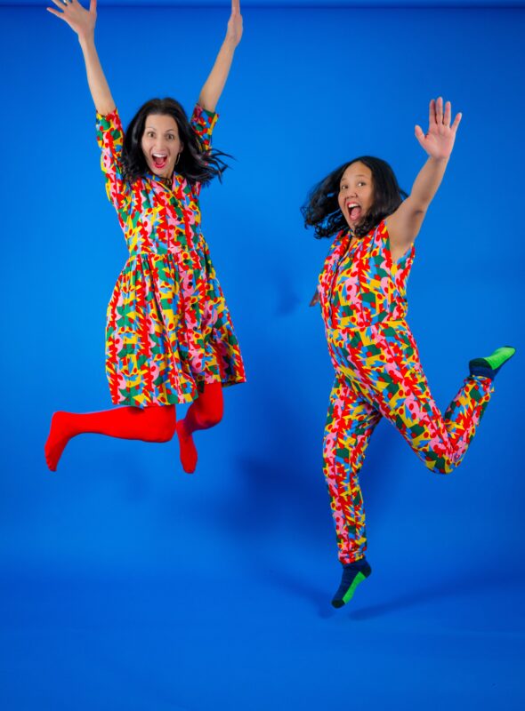 Two people leap joyfully in vibrant, patterned outfits, arms raised in celebration—showcasing creativity that unites our Essex County community.