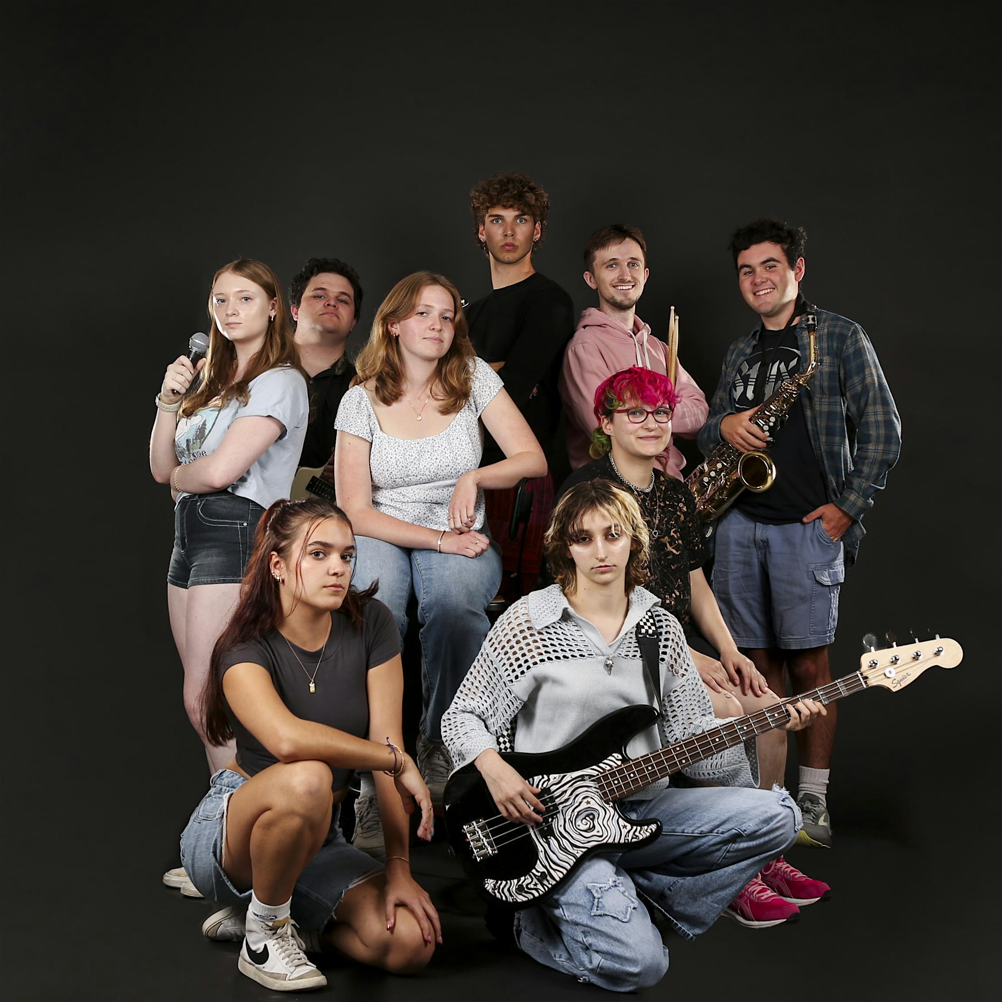 Nine young adults from Essex County beam with creative energy, posing together with instruments, united in musical community.