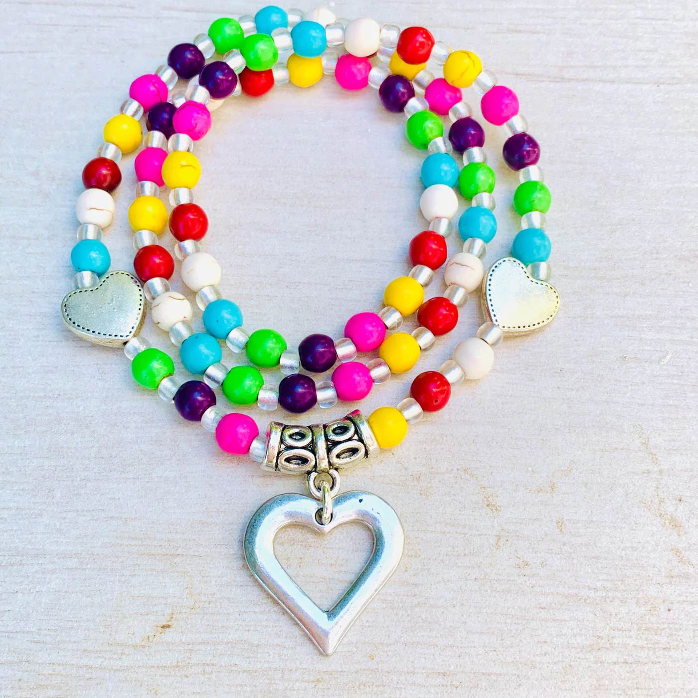 A vibrant bracelet with lively beads and silver heart charms, symbolizing Essex County's creative spirit on a light wood surface.