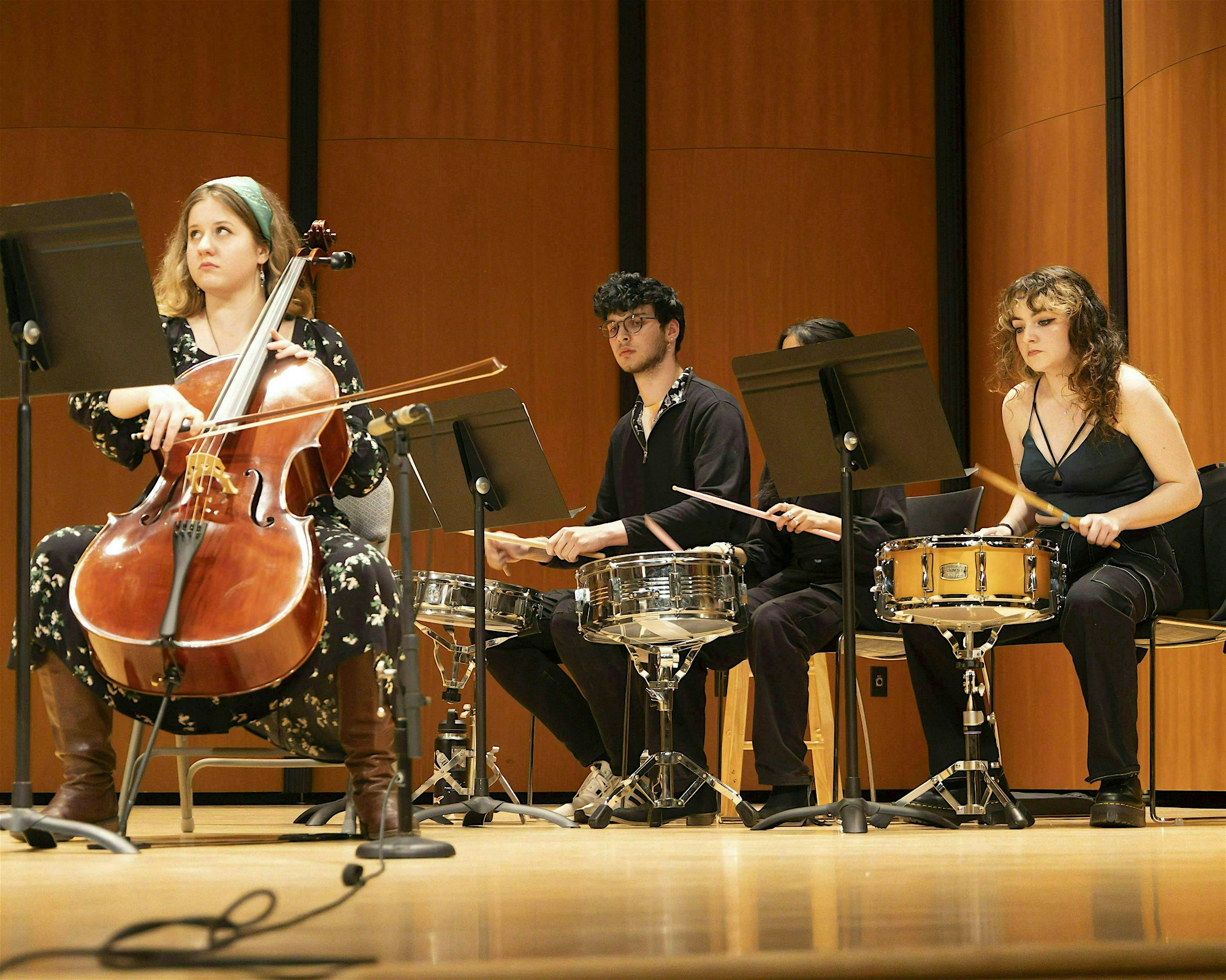 A vibrant group shines on stage as a woman plays cello and three join in on snare drums, uniting Essex County through music.