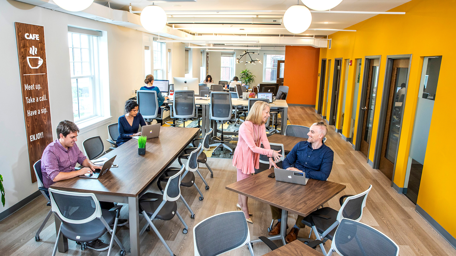 A vibrant Essex County office where people collaborate at bright tables, chat, and create together in a lively, sunlit space.