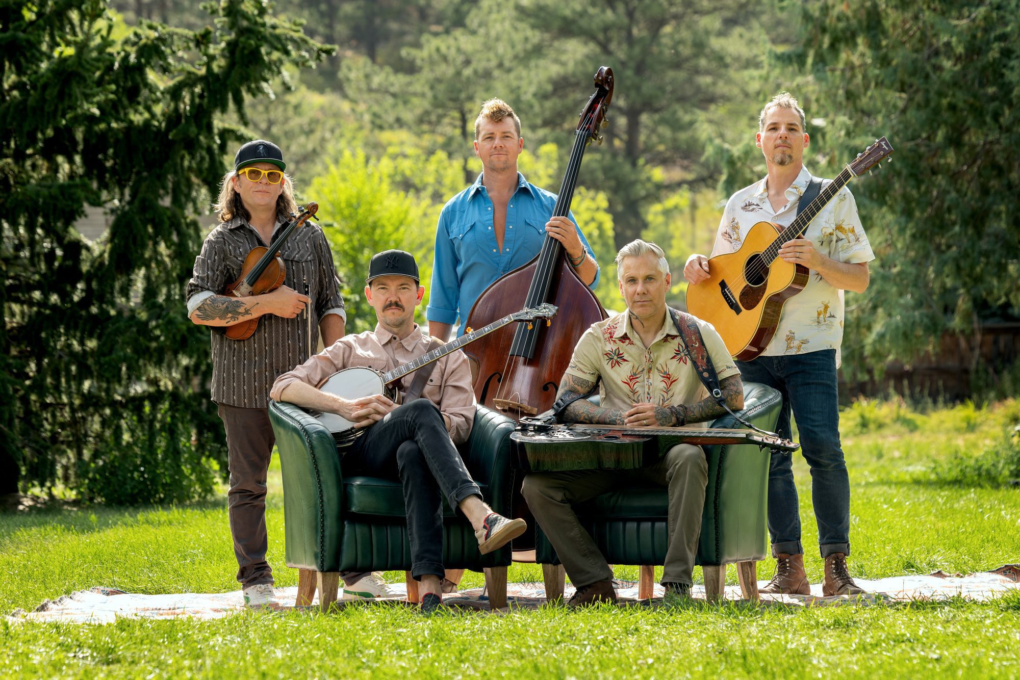 Five Essex County musicians gather outdoors, instruments in hand, radiating creativity and community spirit, united on green grass.