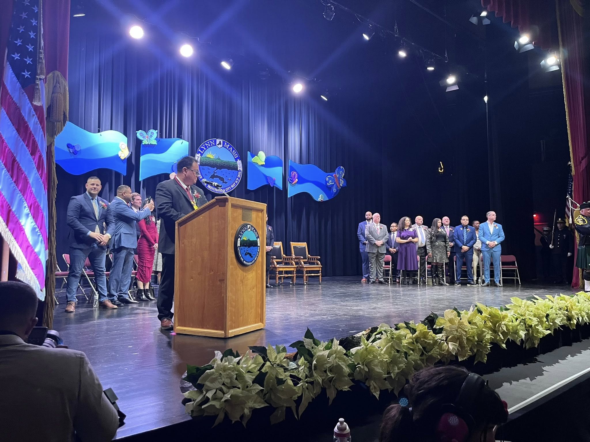 A vibrant speaker energizes the crowd at a flower-filled, blue-bannered stage as Essex County community members unite in celebration.