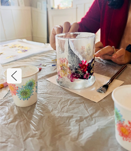 Hands bring pressed flowers to life on a glass at a lively Essex County craft table, with floral cups and paintbrush sparking creativity.