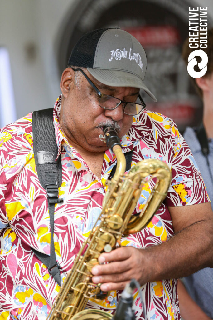 A lively musician in a floral shirt and cap energizes with his saxophone, celebrating Essex County's creative community spirit.