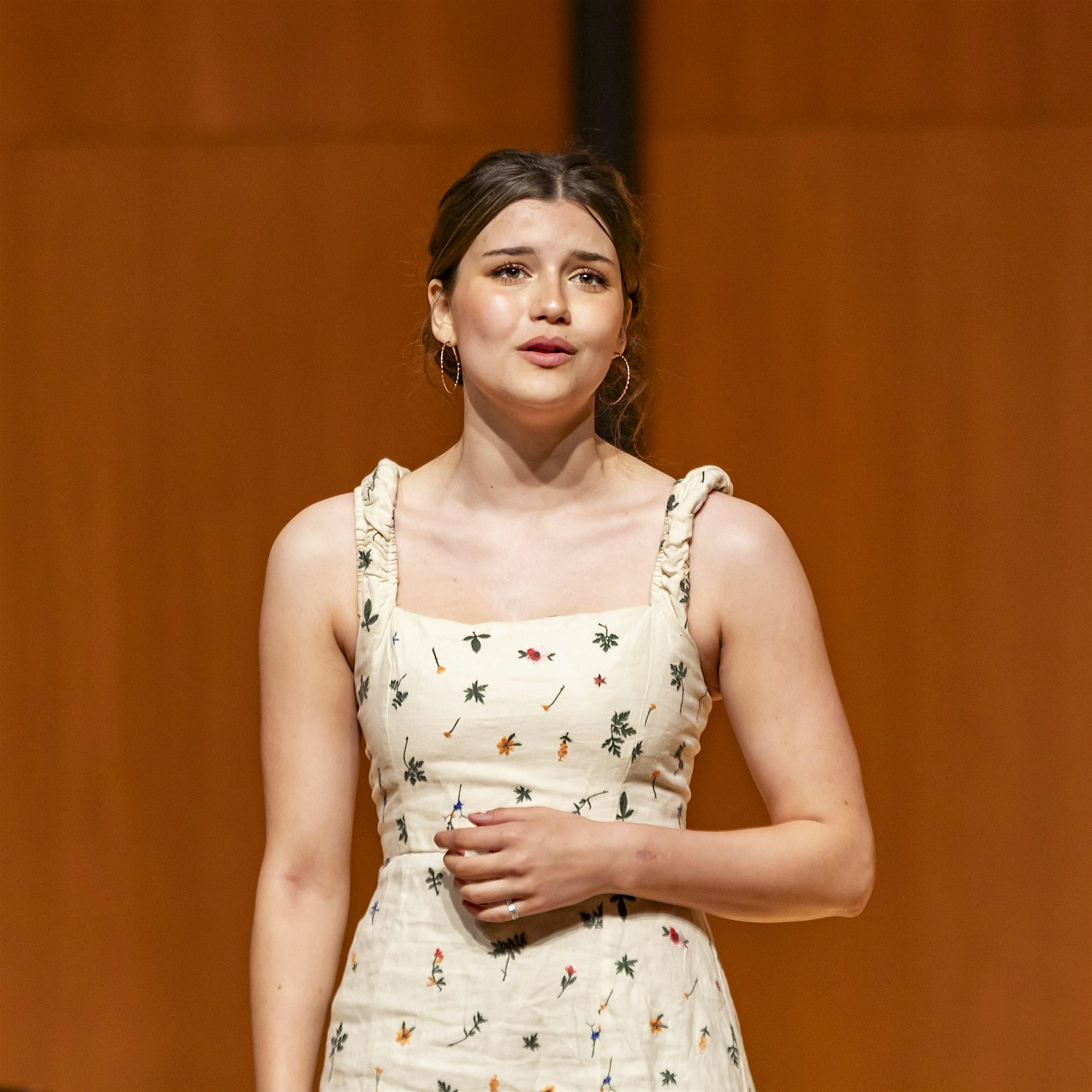 A vibrant young woman in a lively, patterned dress passionately performs against rustic wood, inspiring Essex County’s creative spirit.