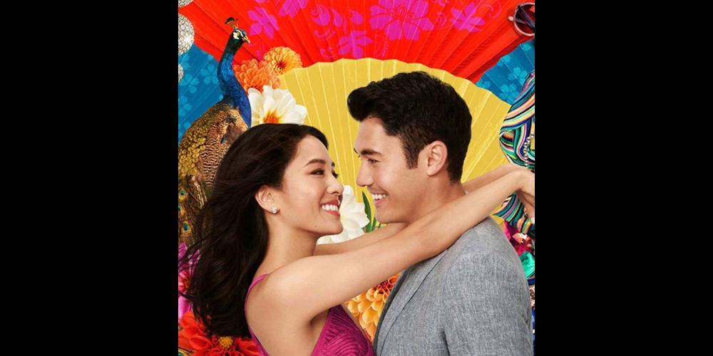 A joyful couple embrace and beam in front of lively, art-filled decor—flowers, a peacock, and a fan—celebrating Essex County’s vibrant spirit.