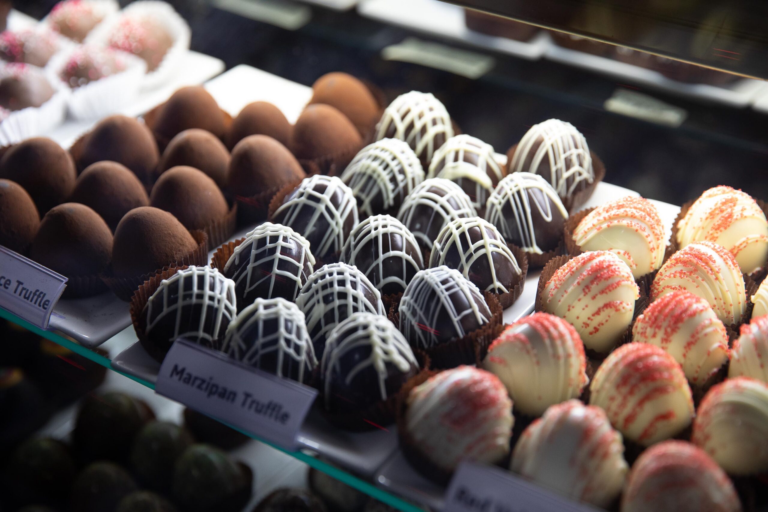 A vibrant case bursts with creative truffles—marzipan, dark, and sprinkle-topped delights—a sweet Essex County community treat!.