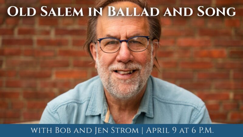 A cheerful, bearded man with glasses beams in front of a brick wall. “Old Salem in Ballad and Song” unites Essex County’s vibrant community; event details below.
