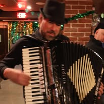An accordionist in a black hat fills a lively Essex County room with Irish music, sparking community spirit and shared joy.