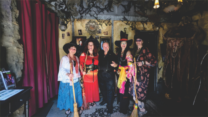 Five adults in creative witch costumes gather in a festive Salem space, celebrating Essex County's spirited small business community.
