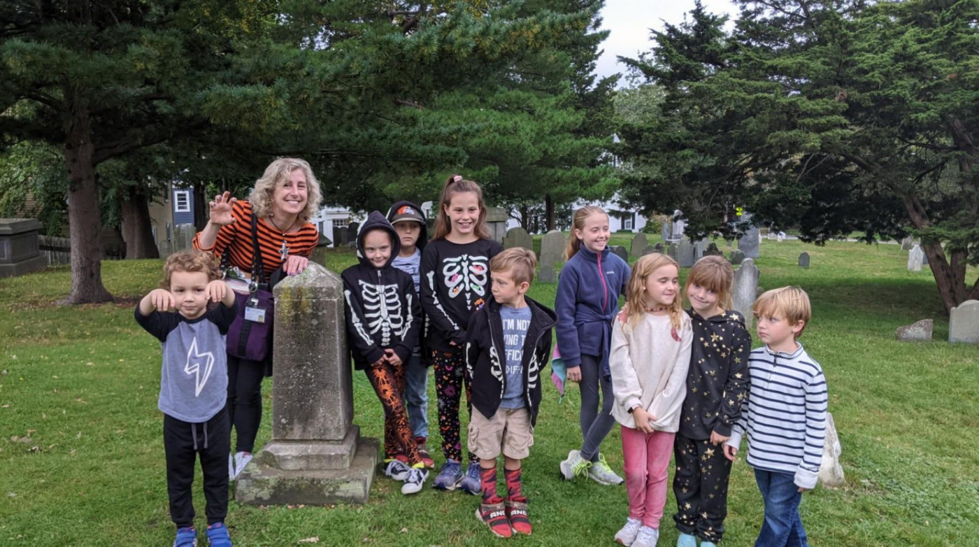 Children and an adult, glowing with smiles in festive Halloween outfits, celebrate community spirit in Salem, MA’s creative Essex County.