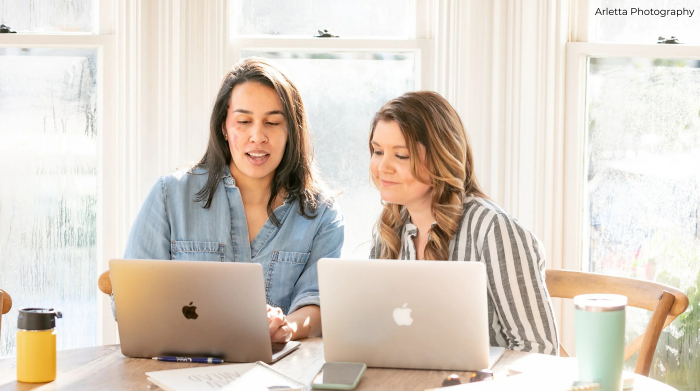Two women collaborate over laptops and coffee, sunlight flooding a vibrant space—Essex County’s entrepreneurs in action.