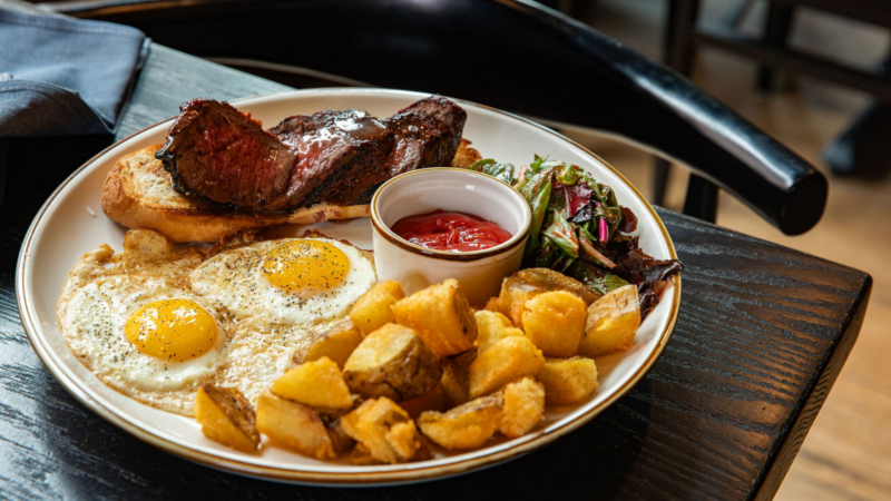 A vibrant plate with sunny-side-up eggs, crispy potatoes, steak on toast, and greens celebrates Essex County’s local flavor and small business creativity.