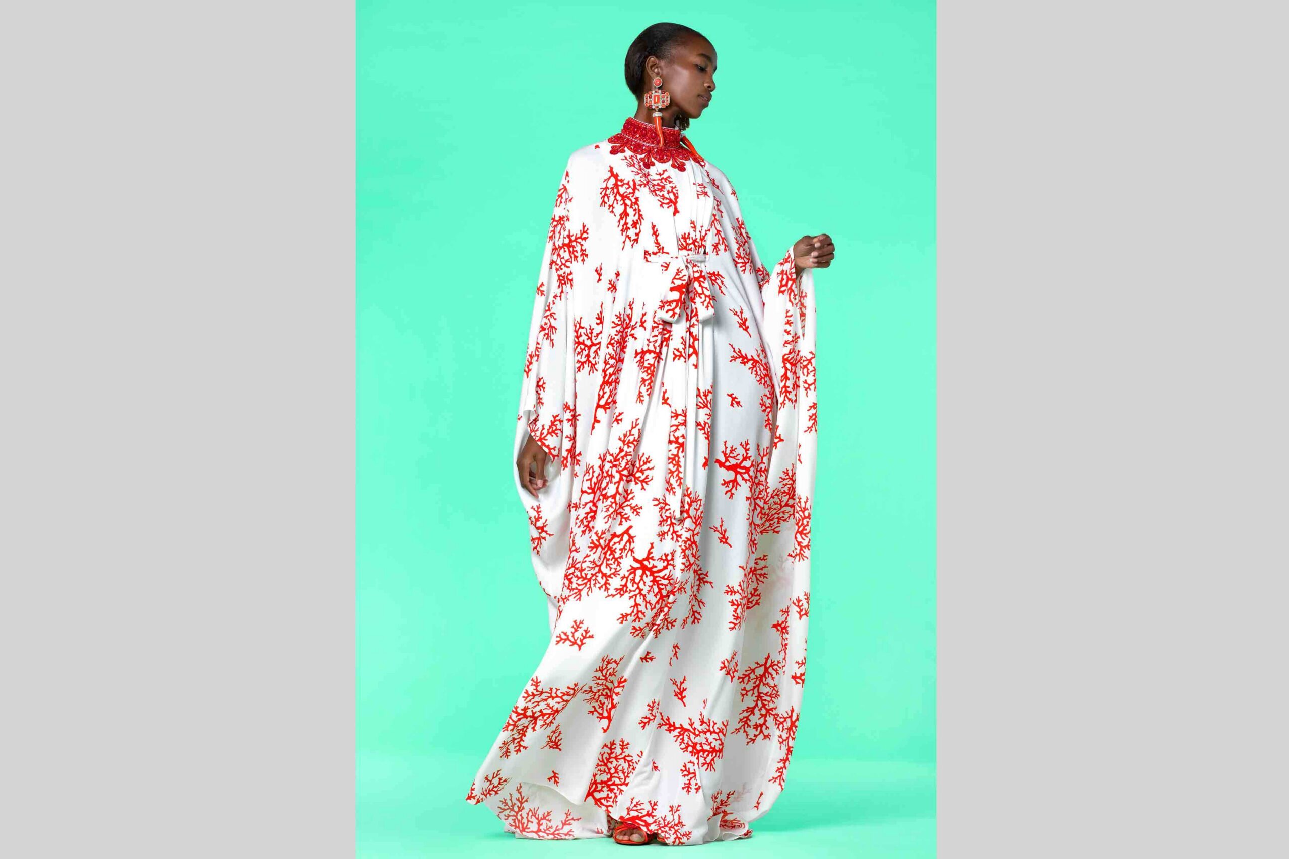 Against a lively green backdrop, a person radiates community spirit in a flowing white dress with red florals—a vibrant style sparking creativity among Essex County’s changemakers.