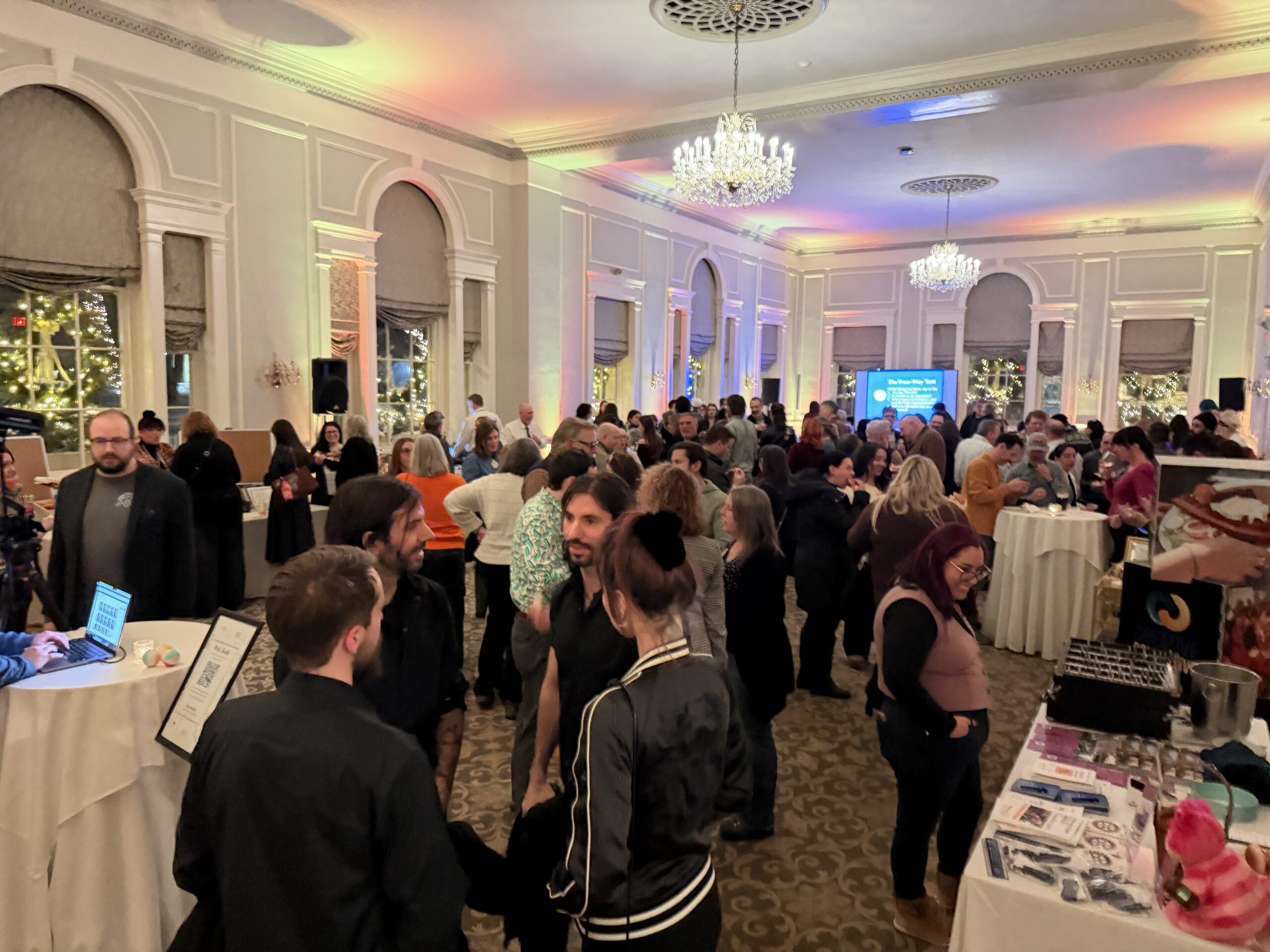 A vibrant crowd exchanges ideas and connections in a bright Essex County ballroom, exploring booths and forming local community bonds.