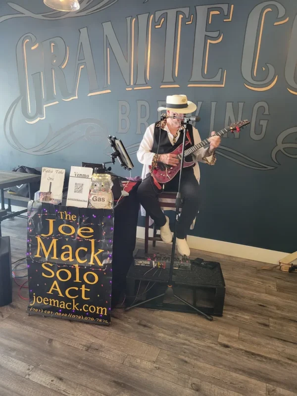 Joe Mack, rocking a hat and shades, electrifies the crowd at a local brewery with soulful guitar and vocals, sparking Essex County’s creative spirit.