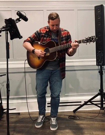 Mike Costanzo energizes an Essex County crowd, strumming his acoustic guitar in a lively, welcoming space filled with music and community.