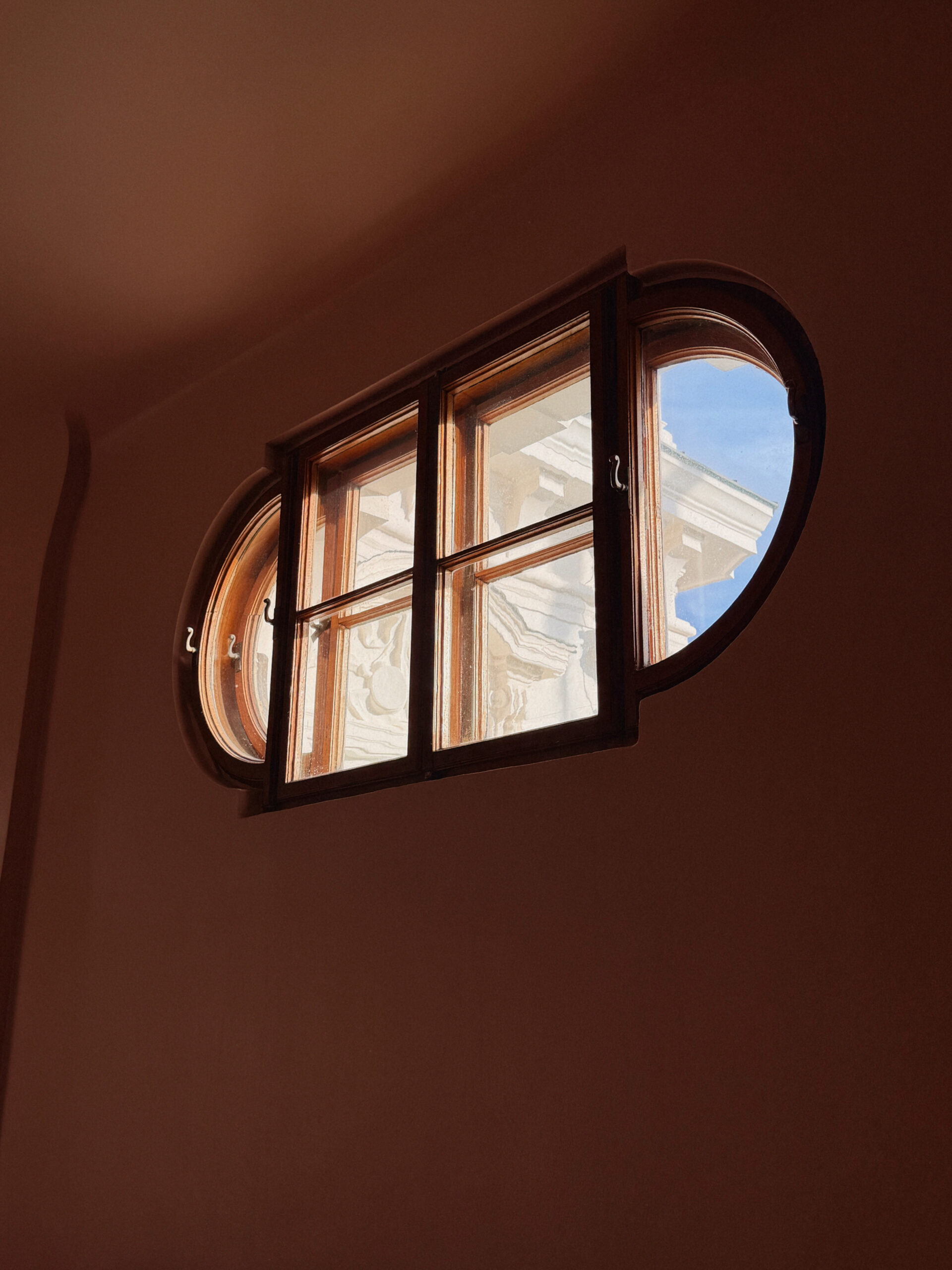 An oval wooden window with four panes frames vibrant sky and lively building details, inspiring Essex County’s creative community spirit.