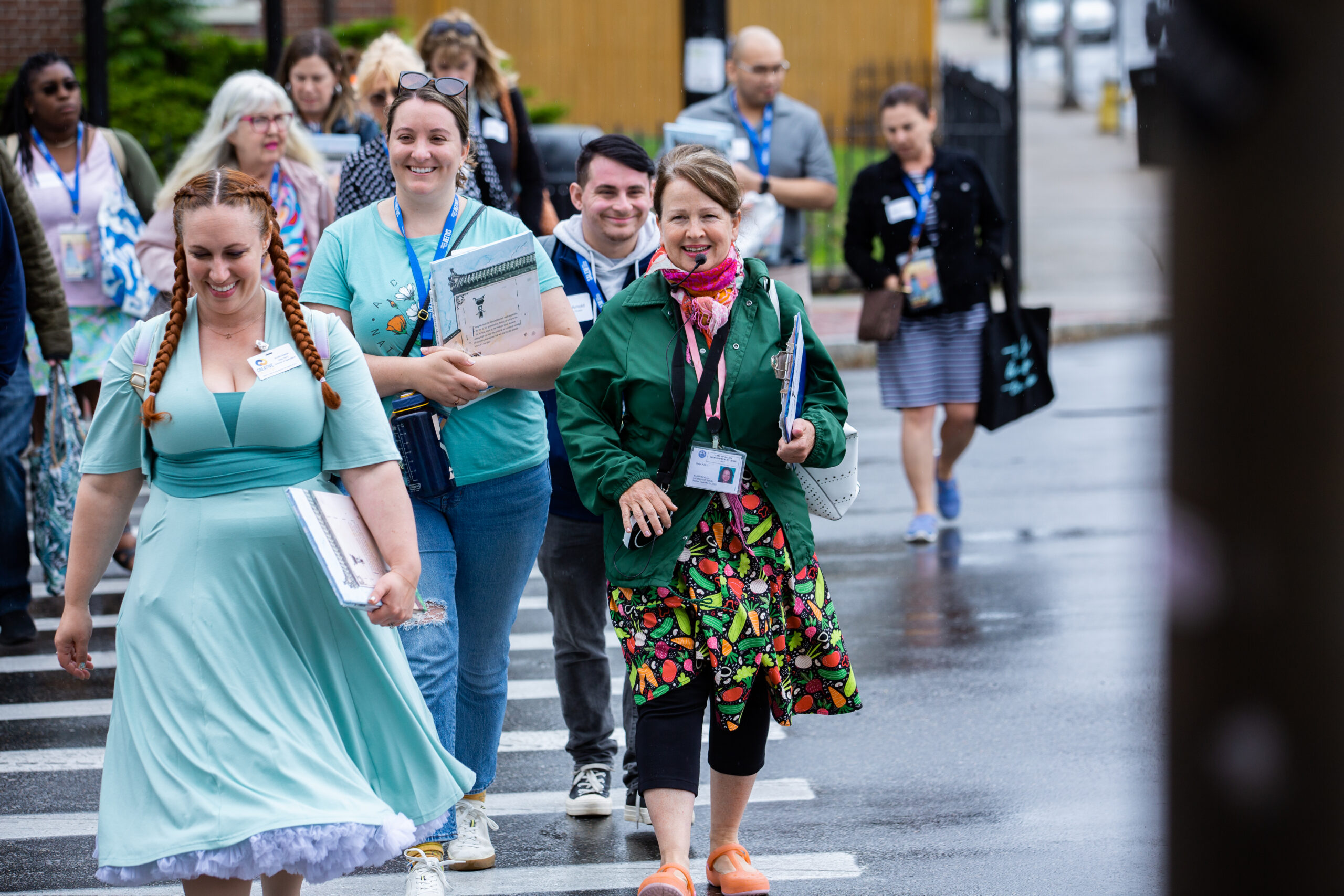 Smiling locals, clutching folders and notebooks, cross a shiny street together—Essex County’s creative community in full stride.