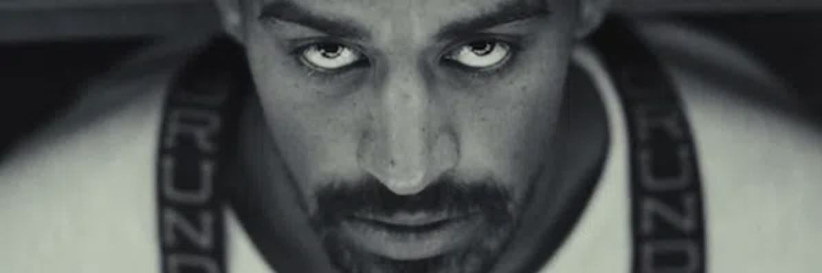 A vibrant man with a mustache and goatee beams up at the camera, his Beverly MA shirt and suspenders celebrating Essex County’s creative spirit.