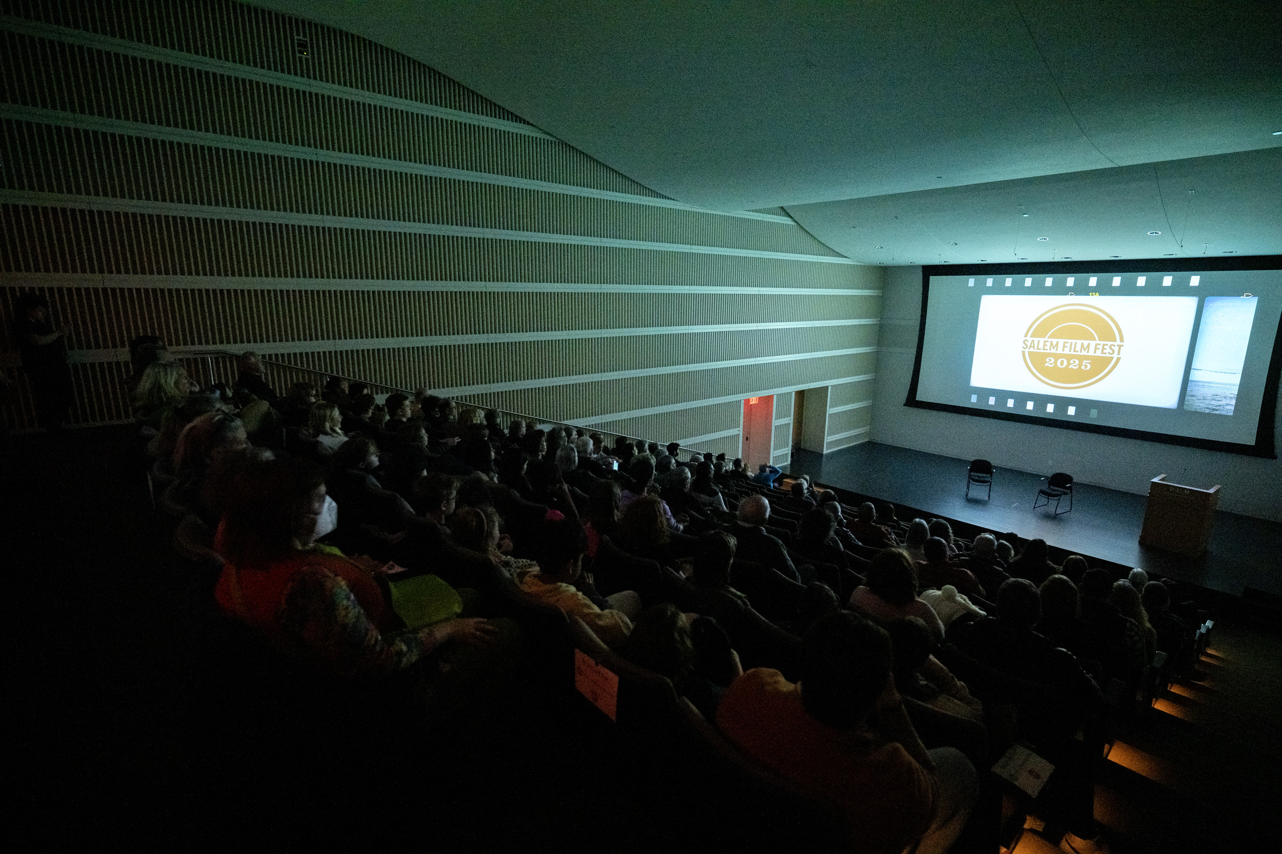 A lively crowd gathers in a stylish, striped-walled auditorium, united in excitement as the Salem Film Fest 2025 lights up the screen—celebrating Essex County’s creative spirit.