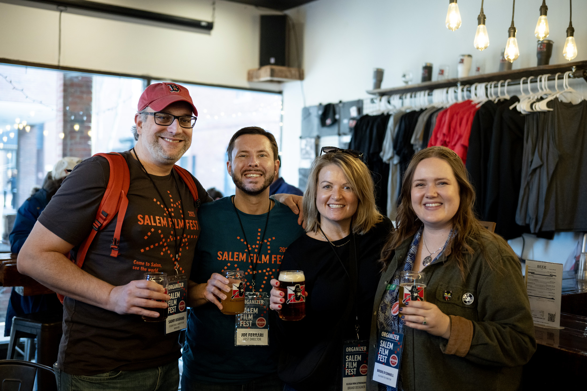Four friends with festival badges share drinks and smiles, celebrating Essex County's creative spirit amid shirts and twinkling lights.