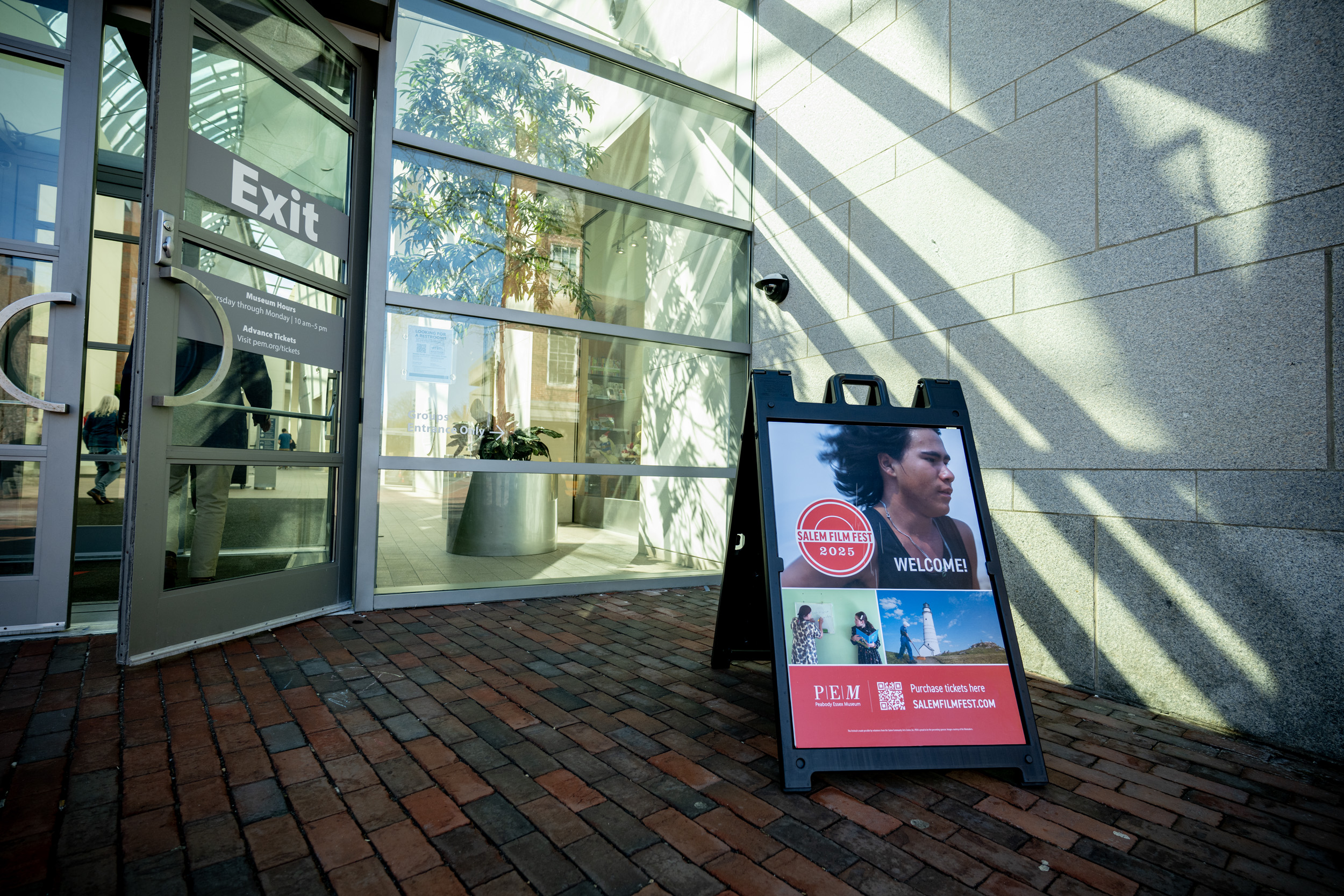 A vibrant sandwich board with lively photos and a cheerful welcome invites our Essex County community outside a sunny glass door.