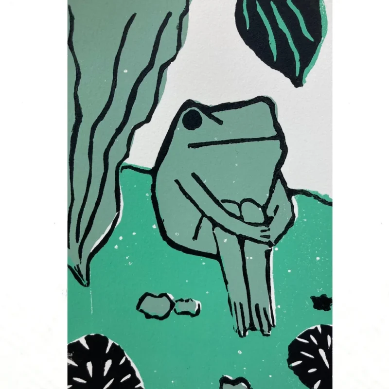 An illustration of a green frog sitting upright with its arms wrapped around its knees. The background includes large green leaves and black-and-white shapes resembling plants or rocks. The style is simple and graphic.